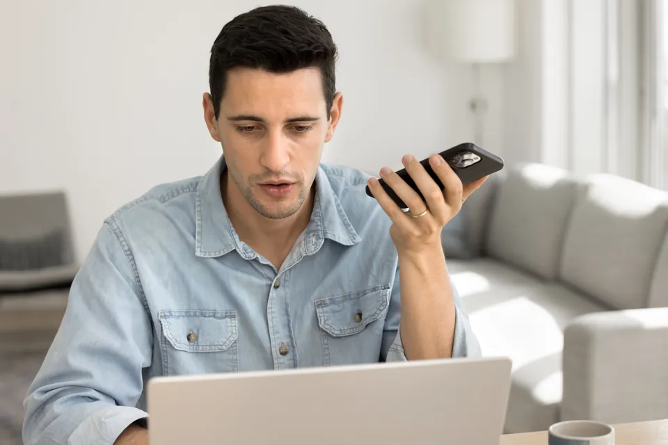 A professional using a phone on speaker beside a laptop